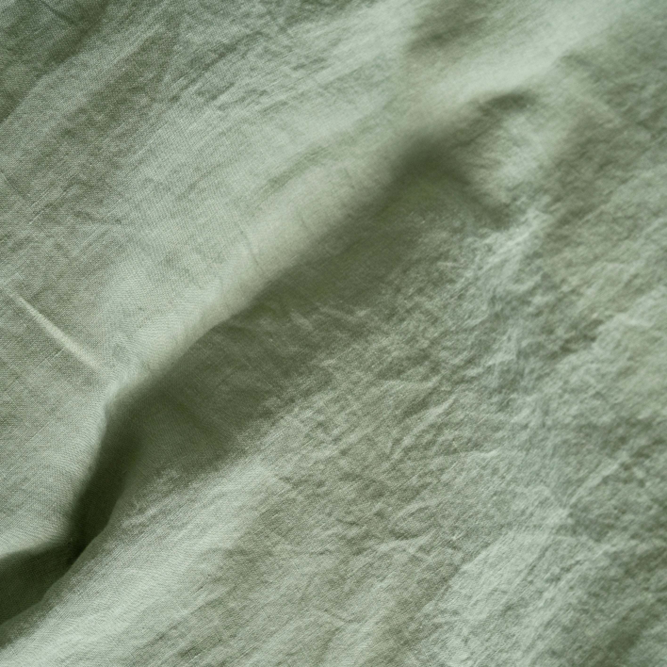 Close-up of textured sage green linen fabric with folds