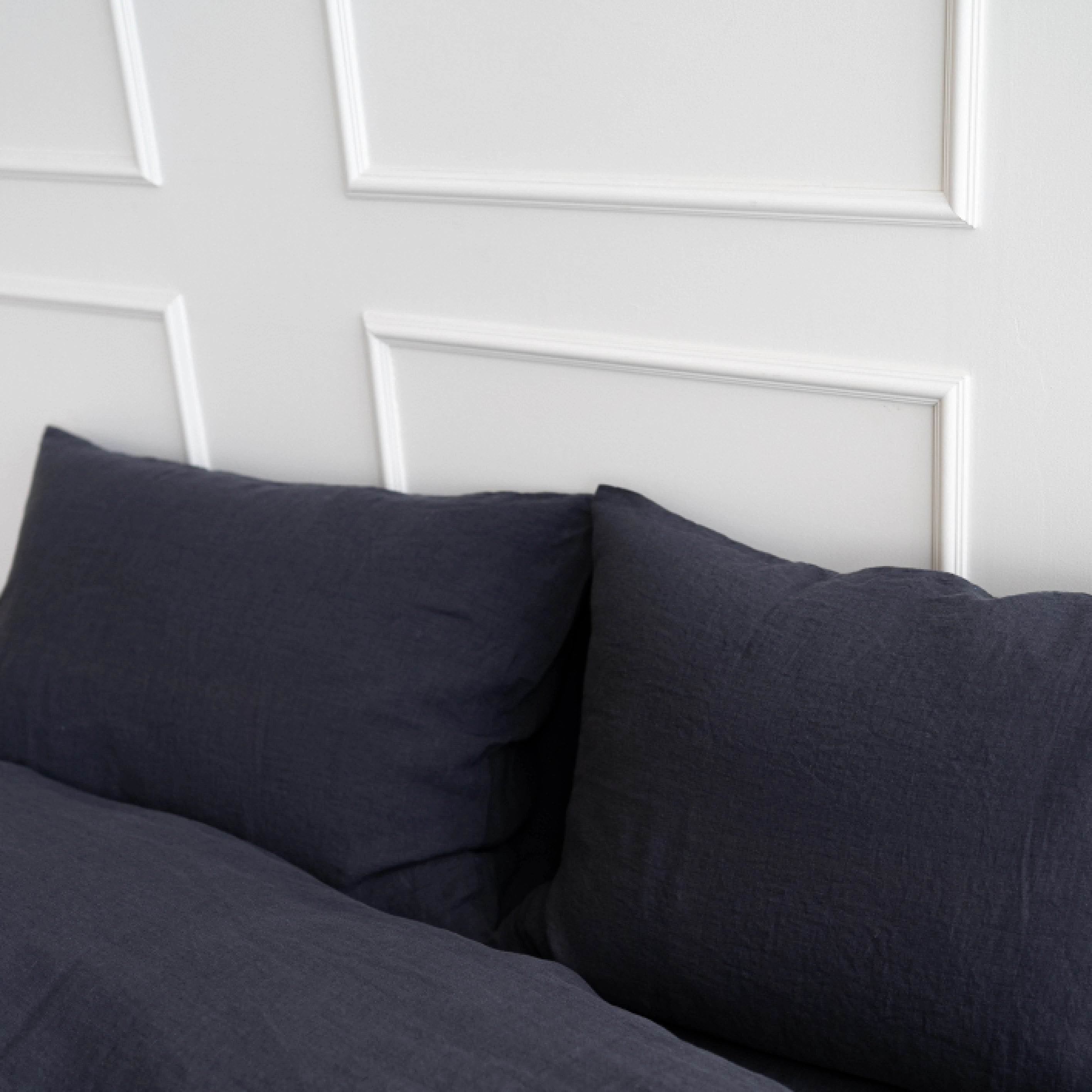 handmade dark grey linen bedding set with pillows on a bed against a white wall.