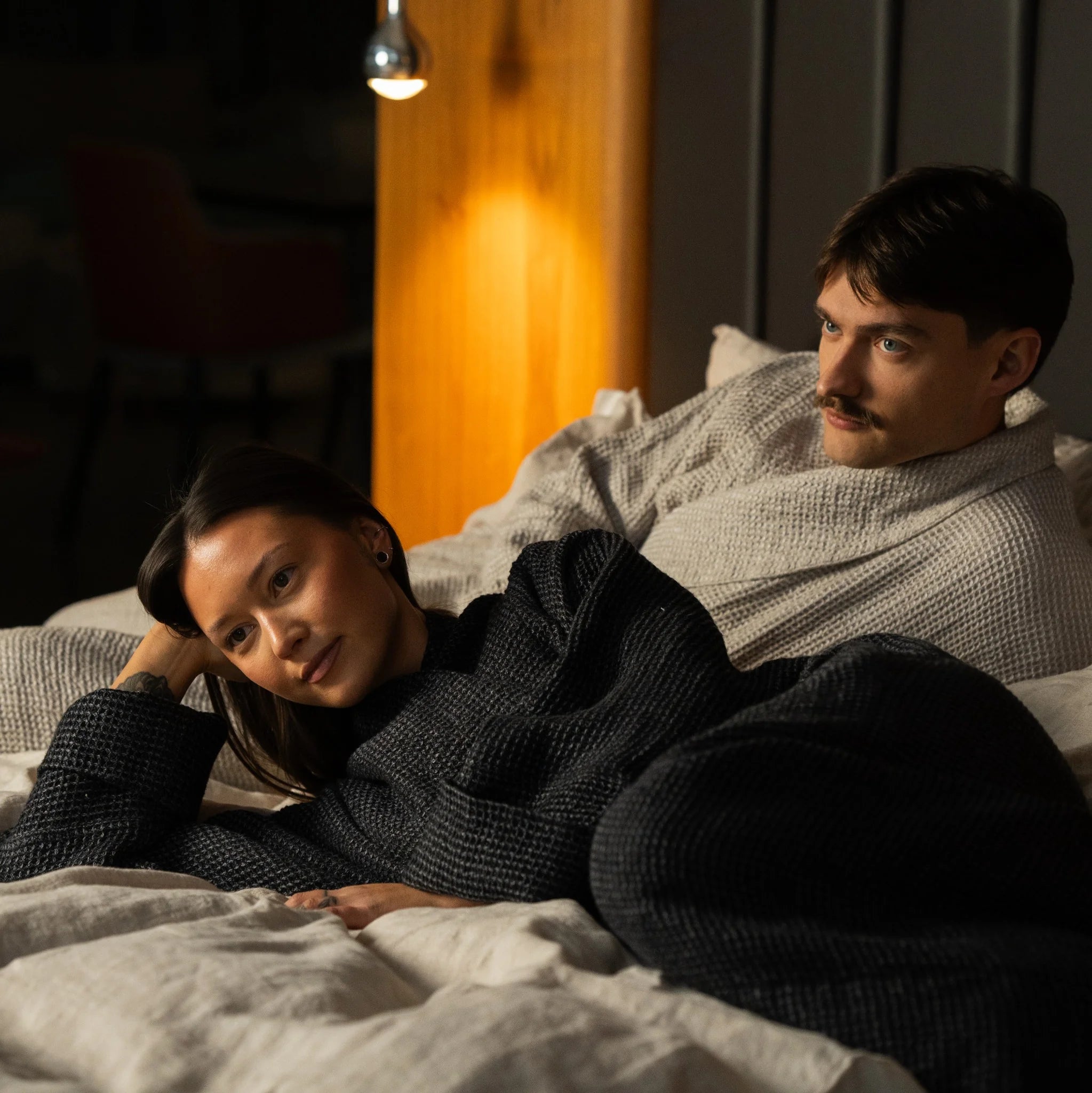 Two people wearing Nommar Atelier Linen Robes resting on linen bedding, expressing calm, intimacy, and a shared slow-living ritual.